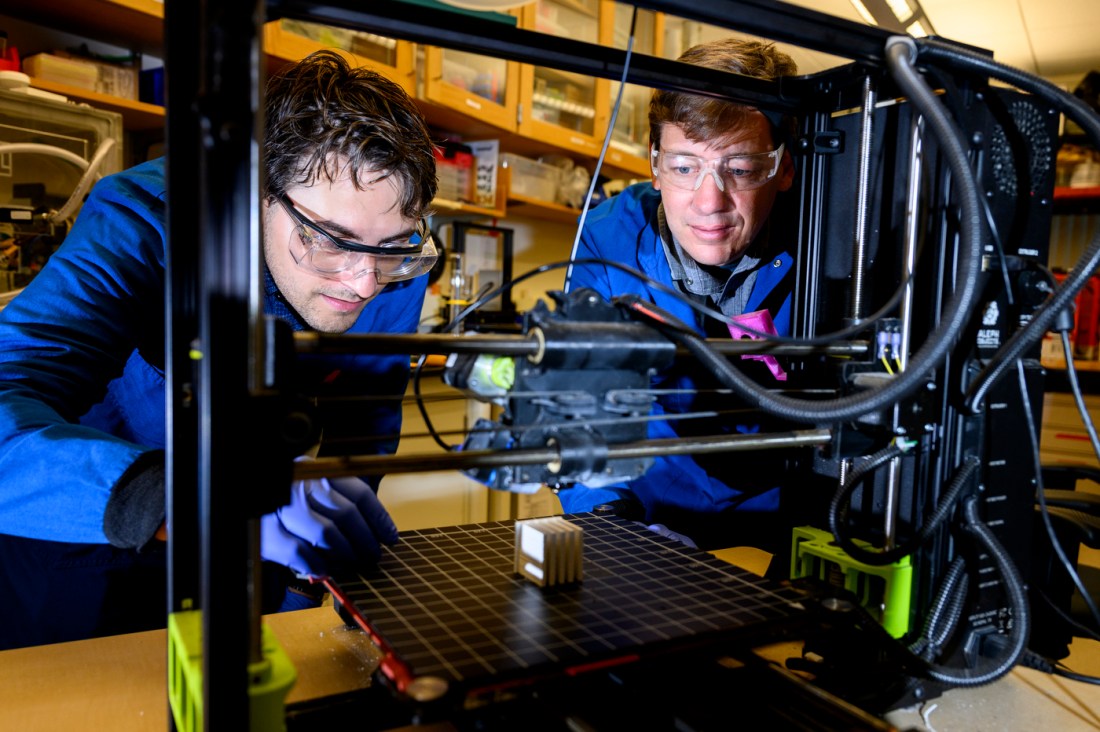 Daniel Braconnier and Randall Erb working with a piece of lab equipment in a lab on the Boston campus.